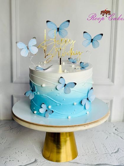 A dreamy blue butterfly cake. The soft blue ombre frosting is adorned with delicate blue butterflies, creating an elegant and serene design for a happy birthday.