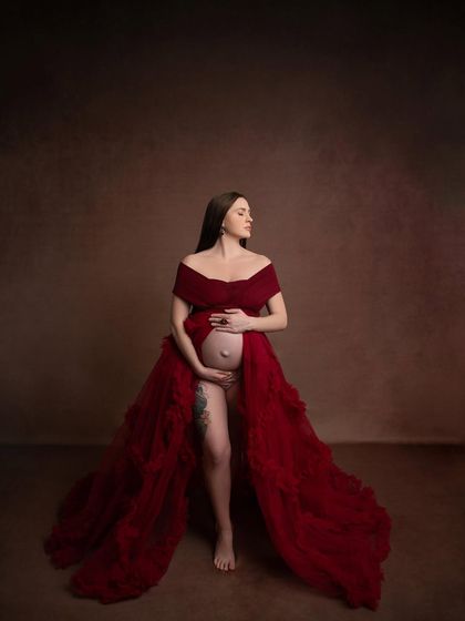 A full-length artistic shot that feels like a painting. The pose highlights the beautiful shape of the pregnant form and the drama of the gown.