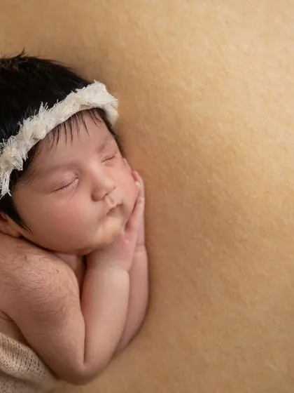A close up of the baby's face, showing the delicate texture of the white lace headband against her dark hair.