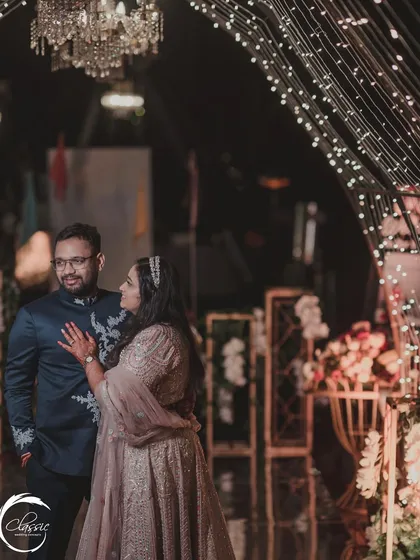 The twinkling lights of the entrance canopy create a beautiful bokeh effect, perfect for capturing romantic moments like this one during the Sangeet night.