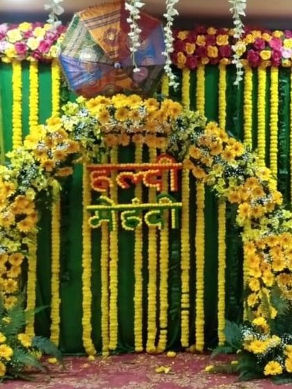 A combined "Haldi Mehandi" backdrop with a floral arch made of sunflowers and marigolds. The green and yellow drapes are complemented by Rajasthani umbrellas, creating a vibrant and traditional look.