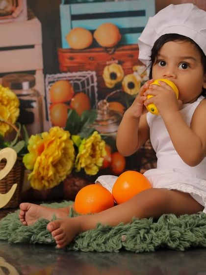 A candid moment from a fruit-themed first birthday shoot. Capturing them as they curiously explore props like lemons and oranges results in the most natural and adorable photos.