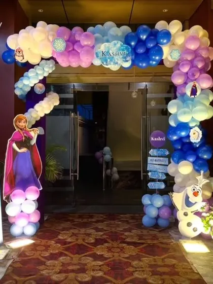 An enchanting entrance for a Frozen-themed first birthday party, with a full balloon arch and life-sized character cut-outs to welcome the guests.