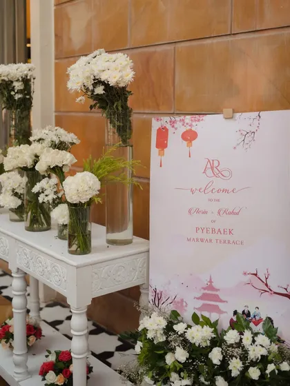 The welcome sign for the Paebaek ceremony, featuring custom artwork that blends Korean motifs with the couple's monogram, directing guests to the Marwar Terrace at The Leela Palace.