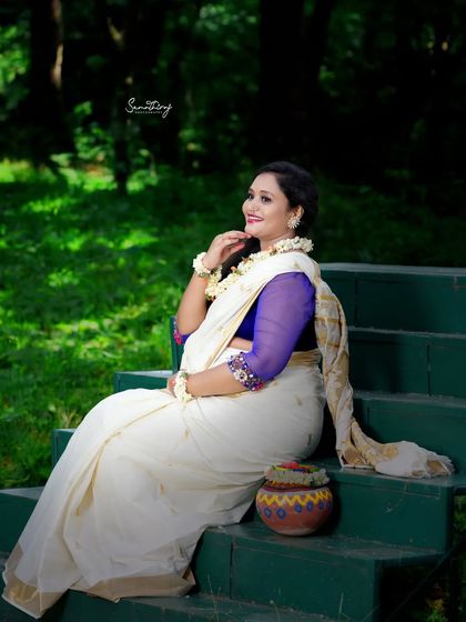A serene outdoor portrait inspired by the mythological character Shakuntala. The mother-to-be is seated on steps in a white saree, surrounded by nature, creating a poetic and timeless image.