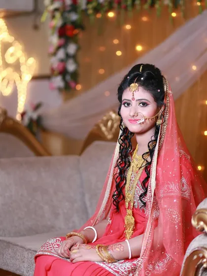 A classic seated portrait of a bride in her beautiful pink and gold wedding attire, looking gracefully at the camera.