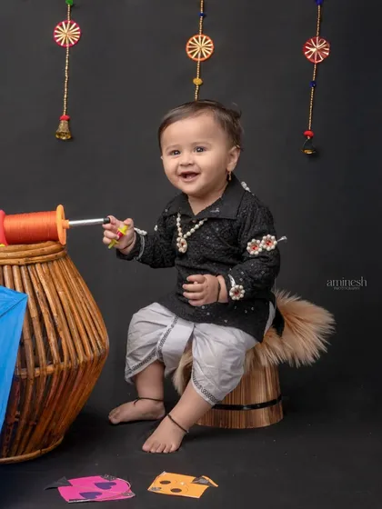 A playful shot from the Makar Sankranti theme, with the baby boy sitting on a small stool next to a blue kite. The setup is perfect for capturing natural and candid moments.