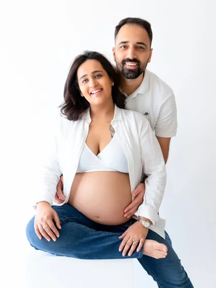 A smiling couple poses for a classic maternity portrait. This shot showcases their happiness and anticipation in a clean, modern studio environment.