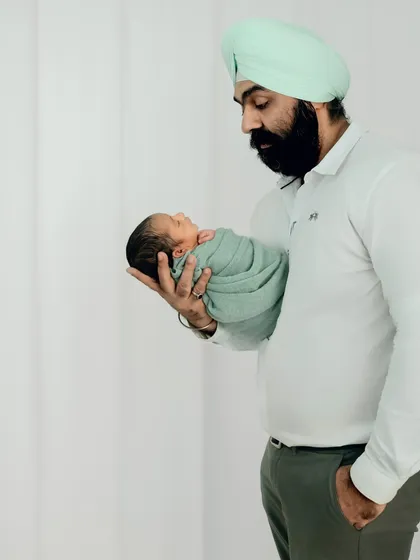 A full-length portrait of a father holding his tiny newborn in one hand, showcasing the contrast in size and the gentle strength of a new dad.