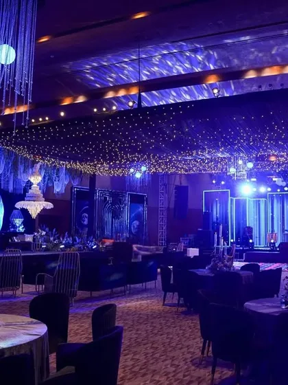 A wide shot of the event hall, showing the dining area in the foreground and the two distinct stage setups, one for the DJ and one for the lounge, all under a sky of fairy lights.