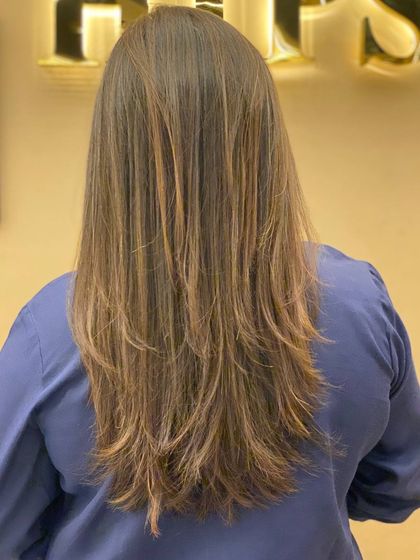 A back view of a client's long, layered hair with a fresh, even color. The style is sleek, healthy, and full of natural movement.
