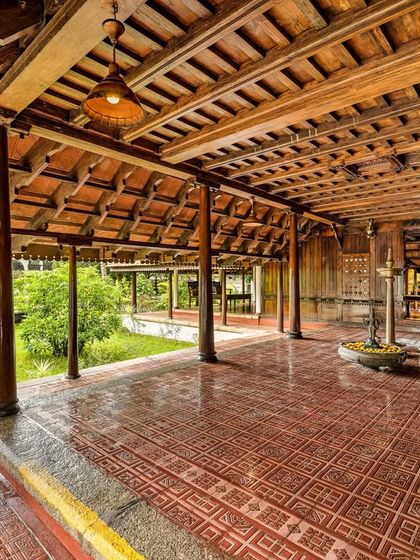 A wide view of the Aranmula Palace reception area, showing the expansive wooden structure and its connection to the lush green lawn outside.
