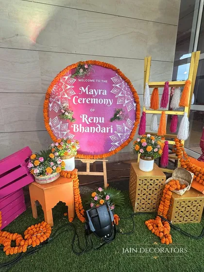 A personalized welcome for a Mayra ceremony. The custom sign is surrounded by bright marigolds, colorful tassels, and painted crates, creating a cheerful and inviting entrance for guests.