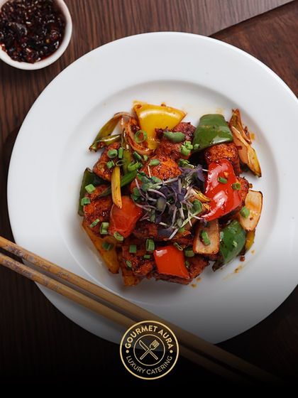 A classic chili chicken dish, beautifully plated with chopsticks resting beside the plate. The vibrant colors of the peppers and garnish make it as appealing to the eye as it is to the palate.
