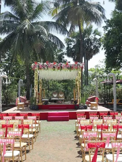 A full view of a classic outdoor wedding setup. The mandap is adorned with pink and white florals, with a red carpet aisle and elegant guest seating, creating a timeless and beautiful ceremony space.