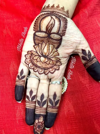 A simple and beautiful design for Diwali, the festival of lights. The palm features a lit diya resting on a lotus flower, with leafy patterns on the fingers, celebrating the spirit of 'Dil-wali Diwali'.