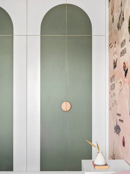 A detail of the custom wardrobe in the kids' room. The doors feature a modern arched design in a soft olive green, with simple circular wooden knobs that are easy for little hands to use.
