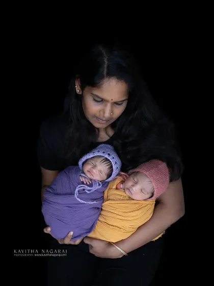 A mother holds her twin newborn babies, each wrapped in a different color. This portrait celebrates the joy and love of having two little ones to cherish.