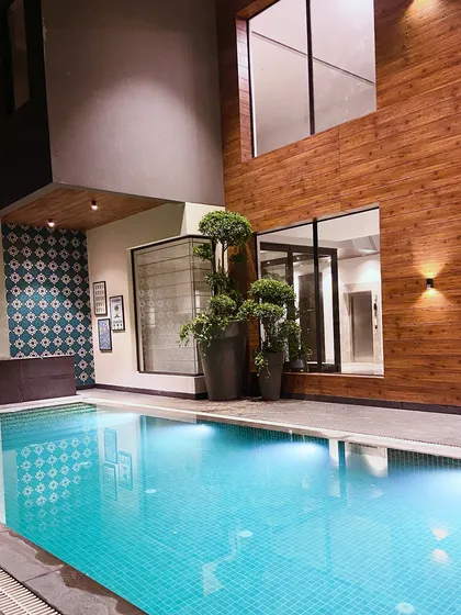 A different view of the pool at night, showing how the lighting highlights the topiary plants and the texture of the wood-paneled wall.