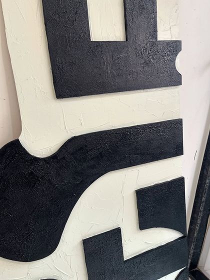 A close-up of the texture on the large black and cream abstract piece. The black sections have a rough, sandy texture that contrasts with the smoother cream background.