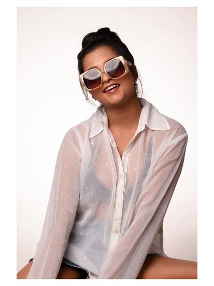 A casual and fun studio portrait. The oversized sunglasses and sheer shirt create a relaxed, summery feel, ideal for a lifestyle or accessory brand.