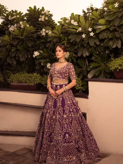 Another full-length view of the purple lehenga, showcasing its beautiful flare against a backdrop of white flowers.