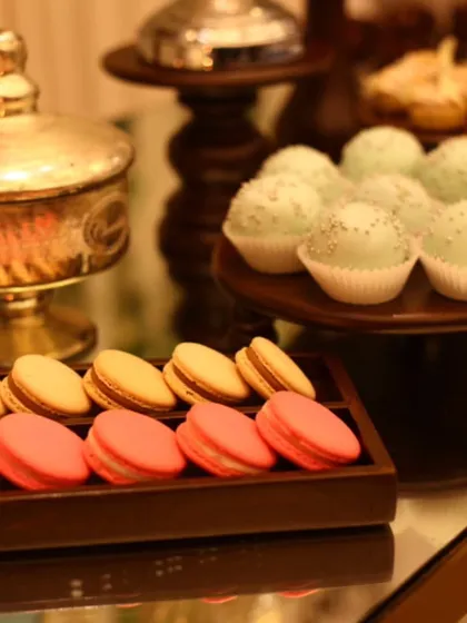 An elegant dessert display featuring trays of pink and yellow macarons alongside delicate cake pops. The arrangement on wooden and glass stands highlights our focus on beautiful presentation.