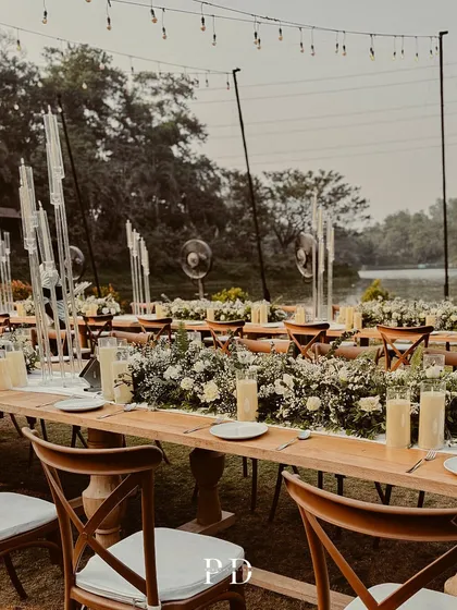 Another view of the stunning lakeside dinner setup, showing the elegant cross-back chairs and the beautiful reflection of the sky on the water.