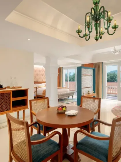 A suite at IHCL Pilibhit House, Haridwar, designed for opulence and comfort. The open-plan living and dining area features a beautiful green glass chandelier and classic wooden furniture, creating a sense of heritage and luxury.