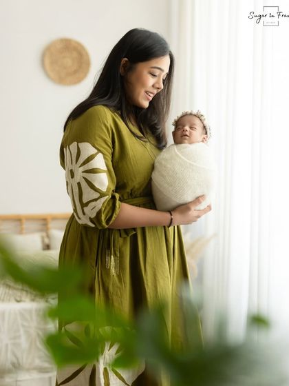 A mother stands by a window, holding her newborn in the soft, natural light. This creates a beautiful, classic portrait with a gentle feel.