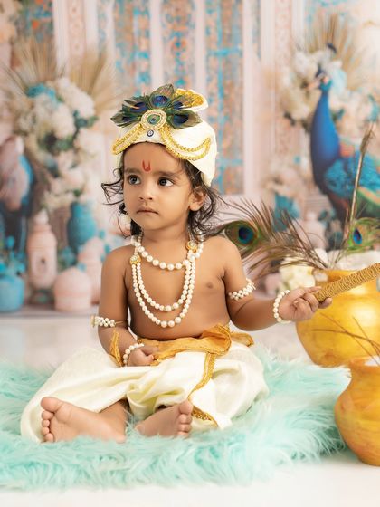 A thoughtful little Krishna holding a peacock feather. The beautiful details of the costume and set come together to create a stunning portrait.