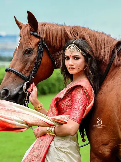 A stunning editorial shot of actress Sauraseni Maitra with a horse. The combination of the traditional red and white saree and the majestic animal creates a powerful and unforgettable image.