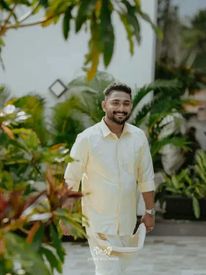 The groom, dressed in a traditional Kerala mundu and shirt, walks with a bright smile, ready to meet his bride.
