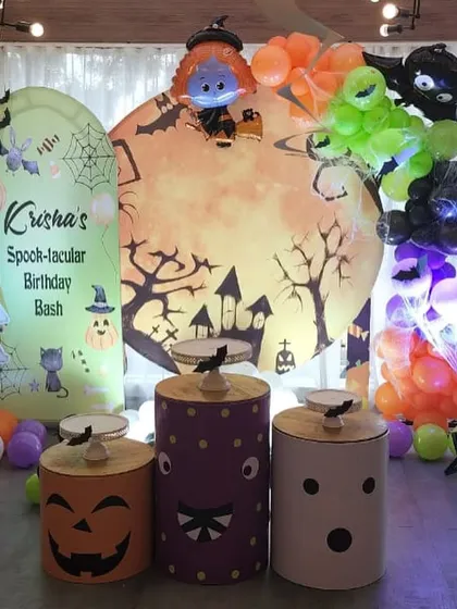 A "Spook-tacular" Halloween themed birthday bash. The decor features a spooky moon backdrop, character cutouts of ghosts and witches, and themed pedestals designed to look like jack-o'-lanterns.