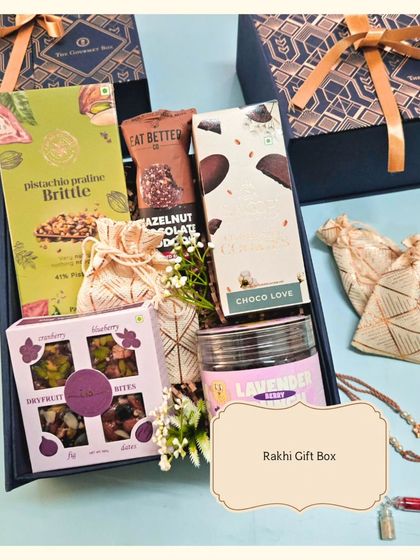 The Rakhi Gift Box in a sophisticated navy blue. This hamper is filled with a delicious assortment of treats like pistachio praline brittle, hazelnut chocolate, and dry fruit bites.
