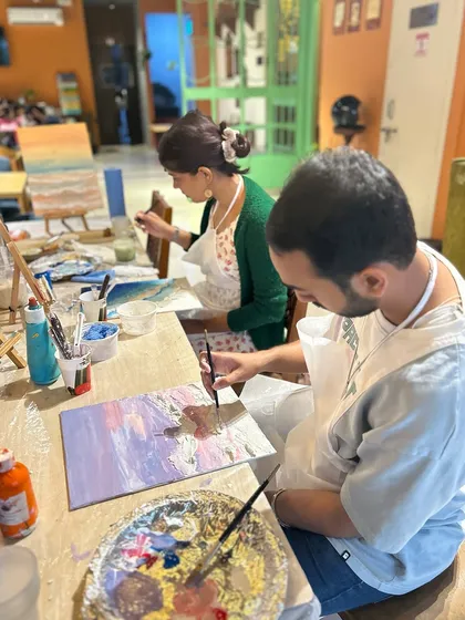 A couple sits side-by-side, each working on their own canvas during a painting workshop. It's a great way to share a creative experience.