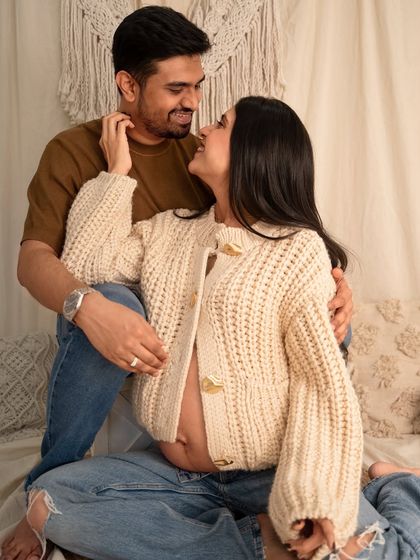A cozy and intimate couple's portrait in a boho-style studio setting. The couple looks at each other with love while seated on a bed, creating a relaxed and natural feel.