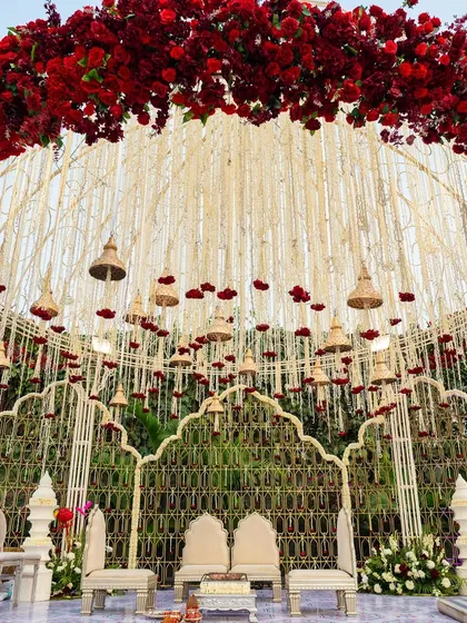 A magnificent mandap featuring a dome of red roses and a cascade of floral strings and temple bells. This design blends traditional motifs with opulent floral artistry for a truly royal wedding ceremony.