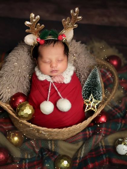 A little reindeer fast asleep. This Christmas-themed newborn portrait is full of festive cheer, with plaid blankets and shiny ornaments.