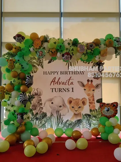 A jungle animal themed party setup featuring a balloon arch with cute animal faces and a personalized backdrop.