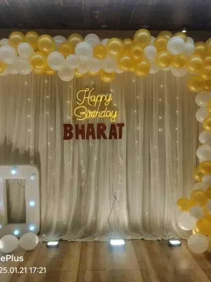 A simple and elegant 70th birthday setup in a banquet hall. We used a white curtain with fairy lights, a gold and white balloon arch, and a "70" marquee number, which works perfectly for any venue.