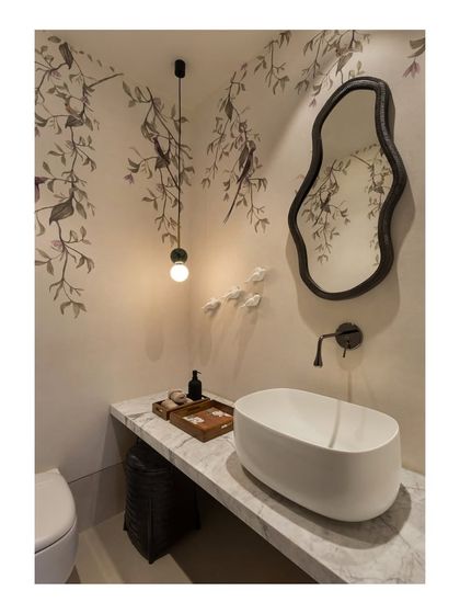 A different angle of the powder room in the House of Terraces, showing the interplay of the wallpaper, the irregular-shaped mirror, and the minimalist pendant light.