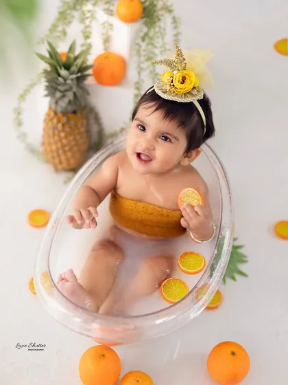Milestone sessions should be full of personality and fun. This delightful nine-month-old is having a blast in a mini bathtub shoot, complete with fresh oranges for a pop of color and playfulness.