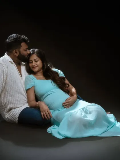 Bathed in soft light against a dark background, this portrait is serene and soulful. The light blue dress adds a gentle pop of color, while their comfortable pose shows a deep and peaceful love.