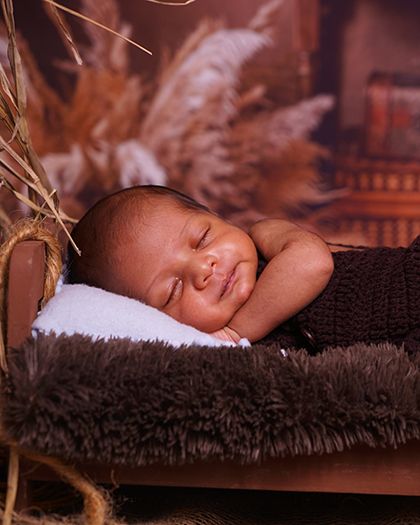 A sweet newborn smiling in his sleep. This rustic, cowboy-themed setup with a soft brown bed is perfect for creating warm and cozy portraits.