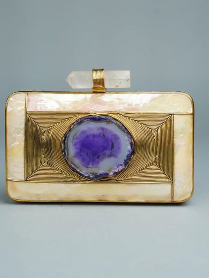A beautiful rectangular clutch featuring a striking purple agate stone as its centerpiece. The stone is set against intricate brass wirework and framed by panels of mother of pearl for a rich, artistic look.