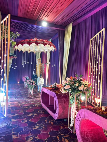 A magical entryway featuring purple draping, illuminated partitions, and suspended Rajasthani umbrellas, creating a pathway that is both regal and whimsical.