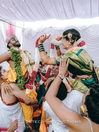 The fun and games of a South Indian wedding. This candid shot captures the bride and groom being playfully lifted on their relatives' shoulders during the garland exchange ceremony.