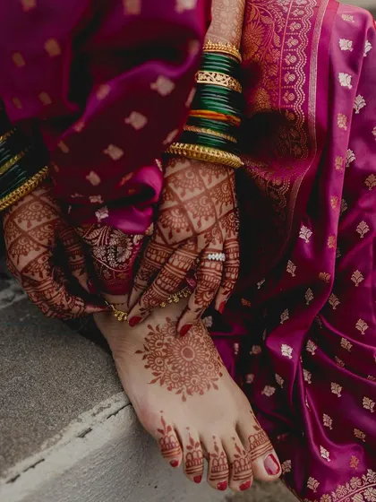 A detailed shot of a Maharashtrian bride's feet and hands, adorned with intricate henna and traditional green bangles.