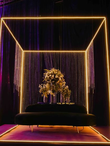 A modern and chic photo booth for a sangeet night. I designed this illuminated neon cube with a backdrop of crystal strings, creating a perfect spot for couples and guests to capture stylish memories. The plush sofa and floral arrangement add a touch of elegance.